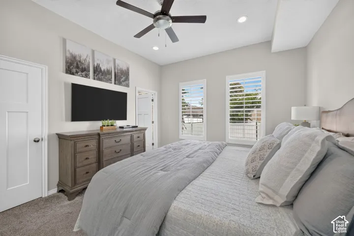 Vaulted ceiling with a ceiling fan, recessed lighting, two windows with plantation shutters, and a paneled door