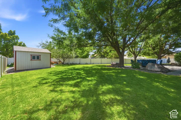 Expansive lawn area, mature trees, white privacy fencing, storage shed with a shingled roof, and a paved patio area