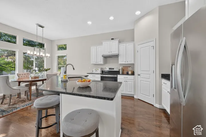 Kitchen featuring a large central island, dark stone countertops, white cabinetry, a stainless steel refrigerator, and wood-finish flooring