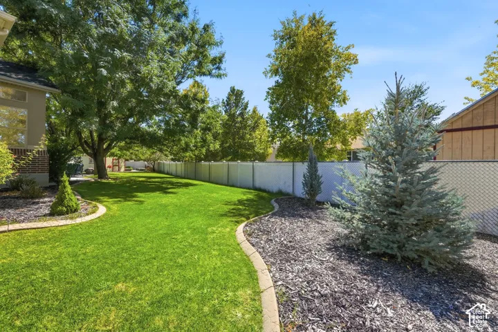 Expansive backyard featuring a manicured lawn, established trees, and a white privacy fence