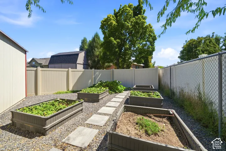 Gravel hardscaping with multiple raised garden beds, paver stepping stones, and a privacy fence