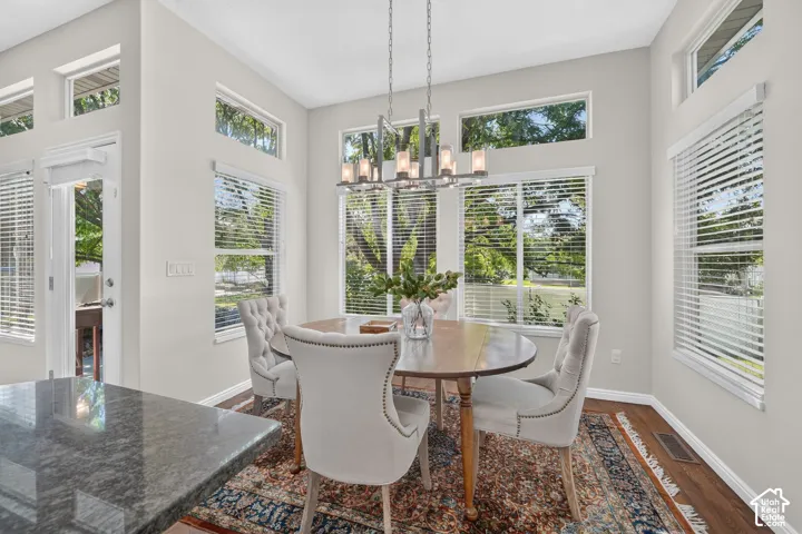 Dining space featuring a modern chandelier, abundant natural light, wood-finish flooring, and a stone-finish countertop