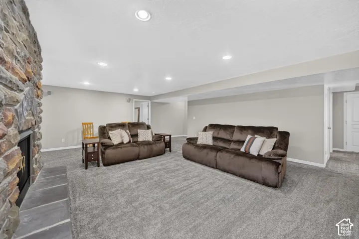 Stone-clad fireplace with a hearth, recessed ceiling lighting, light gray wall finishes, and gray carpeting
