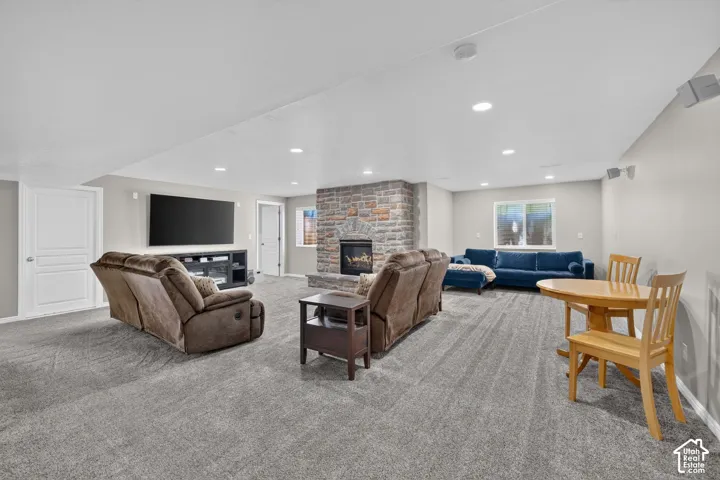 Spacious room featuring plush gray carpeting, recessed ceiling lighting, a stone-clad fireplace, and multiple windows