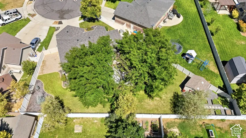 Expansive property with a privacy fence, mature trees, landscaped garden beds, and a paved patio area