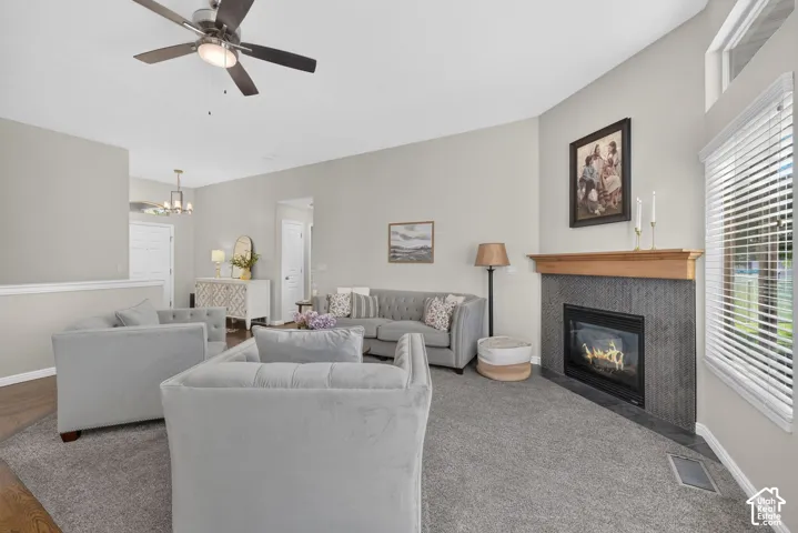 Corner fireplace with a wooden mantel and dark tile surround, ceiling fan with integrated lighting, wood-finish flooring, and upper transom windows