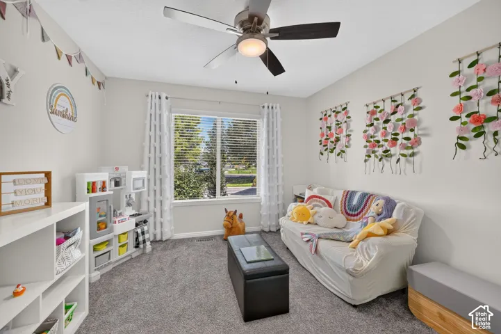 Carpeted room with a ceiling fan, a window featuring horizontal blinds and curtains, and white built-in shelving