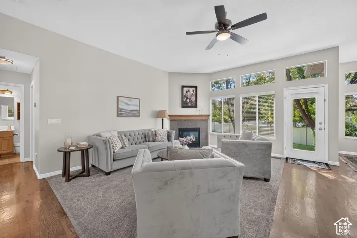 Spacious living area featuring a fireplace with a wood mantle, an overhead ceiling fan, and hardwood flooring