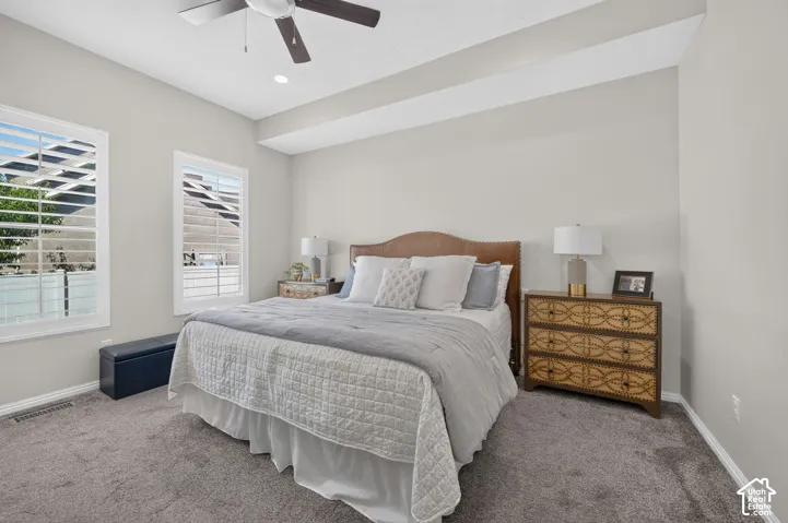 Wall-to-wall carpeting, two windows with plantation shutters, ceiling fan with integrated lighting, recessed lighting, and a tray ceiling