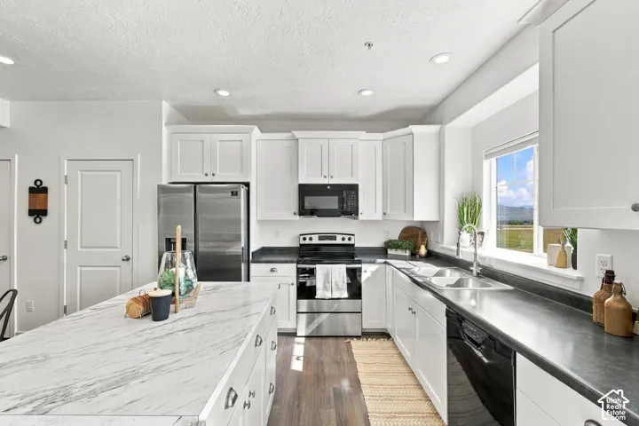 Kitchen featuring white cabinetry, stainless steel appliances, a large center island with a stone-finish countertop, dark countertops, and wood-finish flooring