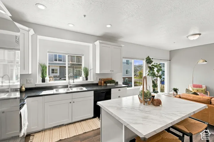 Kitchen featuring recessed lighting, white cabinetry, dark countertops, a stainless steel double basin sink, and a kitchen island with a light-toned countertop