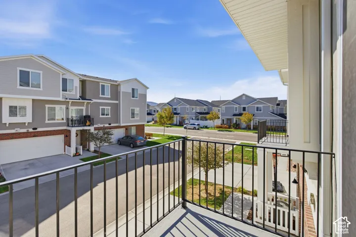 Balcony with black metal railings, overlooking a paved drive, manicured lawn, and multi-story townhomes with garages