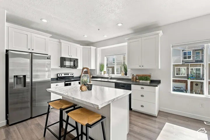 Kitchen featuring white shaker cabinetry, dark countertops, a stainless steel refrigerator, and wood-finish flooring
