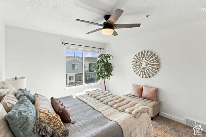 White walls with a textured ceiling, a window with dark curtain rod, and a multi-blade ceiling fan with integrated lighting