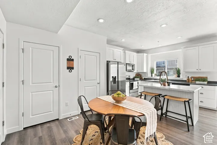 Open-concept kitchen featuring white cabinetry, stainless steel appliances, a center island with seating, and wood-finish flooring