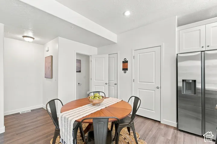 Wood-finish flooring, recessed lighting, white shaker-style cabinetry, and stainless steel refrigerator