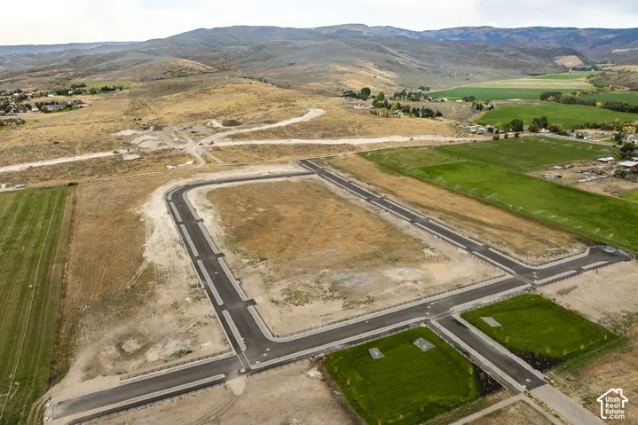 Developed road infrastructure with curbs, multiple building lots, surrounding open land, and distant hills