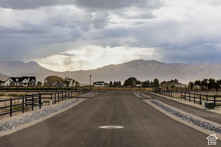 Paved road with gravel shoulders leading to a development featuring homes with mountain scenery