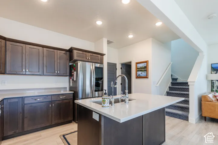 Kitchen featuring dark wood-finish cabinetry, stainless steel appliances, and a central island with an undermount sink and light-toned countertop