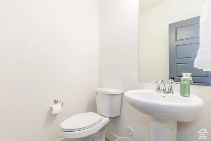 White pedestal sink with chrome faucet, white toilet, and a wall-mounted mirror