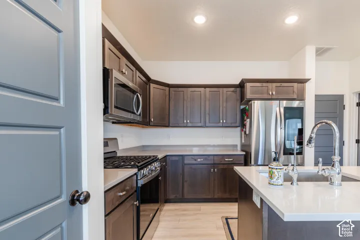 Stainless steel appliances, recessed lighting, wood-finish flooring, white countertops, and dark wood cabinetry
