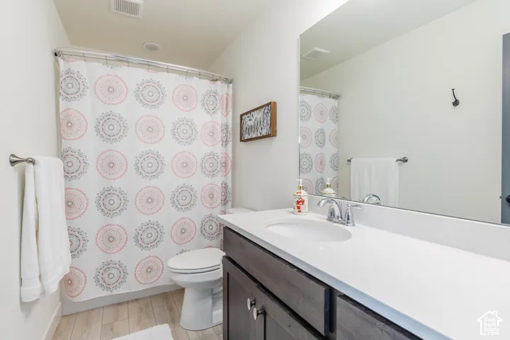 White vanity countertop, chrome faucet, undermount sink, wood-finish vanity cabinetry, and wood-finish flooring
