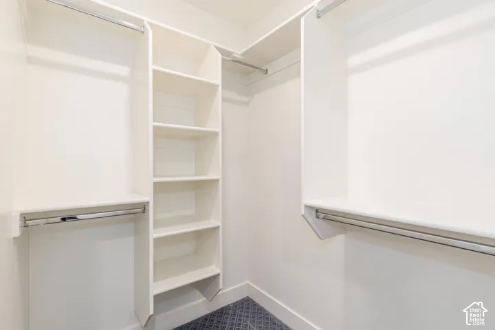 Custom closet organization system featuring white shelving, multiple hanging rods, and patterned carpet flooring