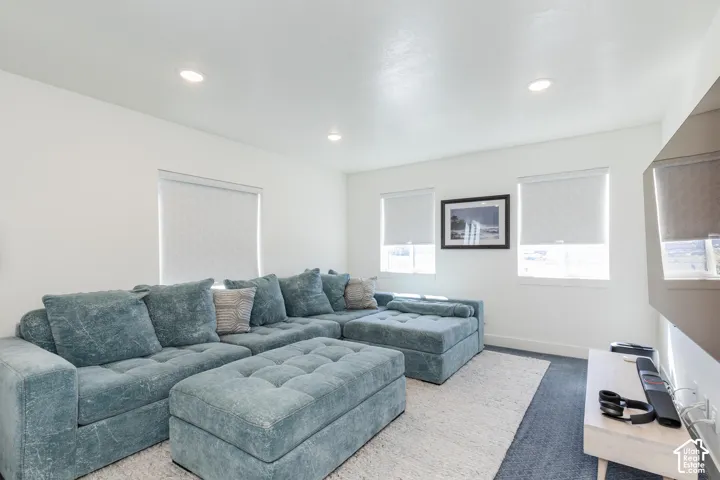 Recessed ceiling lighting, white walls, multiple windows with roller shades, and dark carpet flooring