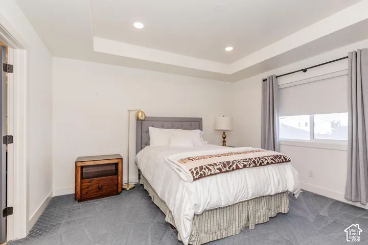 Tray ceiling with recessed lighting, carpeted flooring, window with roller shade, and drapery rod with curtains