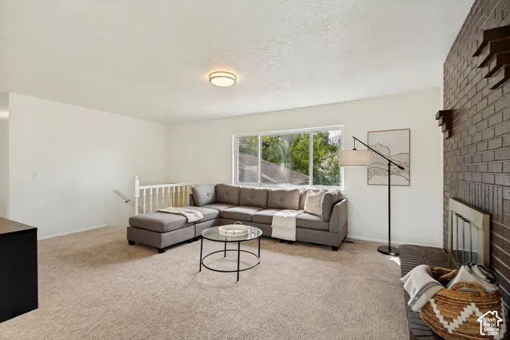Living space featuring neutral carpeting, a large window, a brick-faced fireplace, and white painted walls