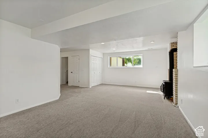 Spacious room featuring light gray carpet, recessed lighting, white walls, and a brick-faced wood-burning stove