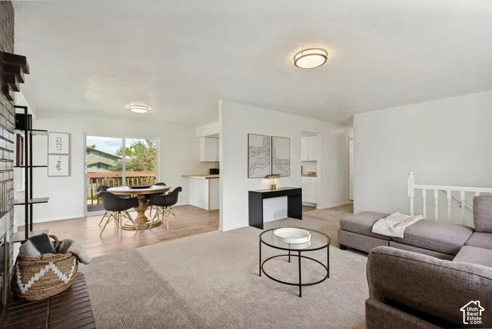 Open-concept living area with light wood-finish flooring, a brick-faced hearth, and sliding glass door access to an exterior deck