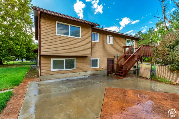 Two-story exterior with horizontal siding, multiple windows, a wood deck with stairs, a sliding glass door, and a concrete patio