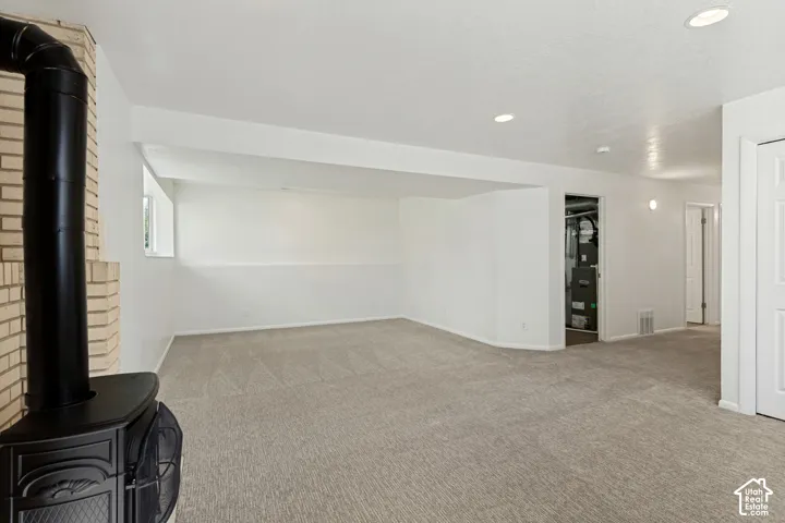 Spacious carpeted room featuring a wood-burning stove with a brick surround, recessed lighting, and a window for natural light