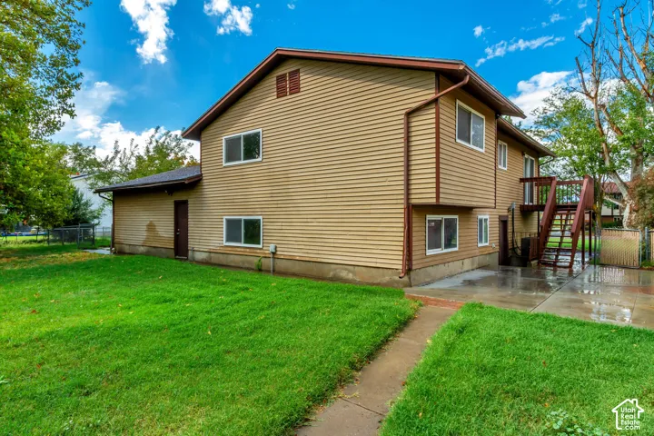 Exterior featuring tan siding, multiple windows, an exterior staircase leading to an upper-level balcony, and a concrete patio