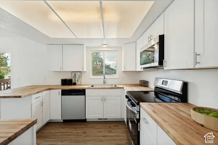 Kitchen featuring white cabinetry, light wood-finish countertops, stainless steel appliances, and wood-finish flooring