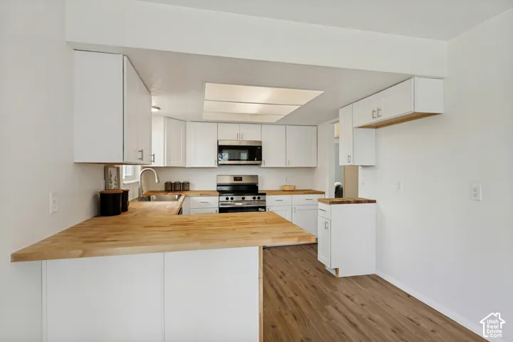 Kitchen featuring white cabinetry, wood-finish countertops, stainless steel appliances, and wood-finish flooring