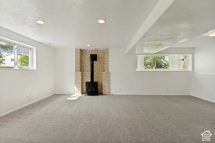Spacious room featuring light gray carpet, recessed lighting, and a brick-backed wood-burning stove