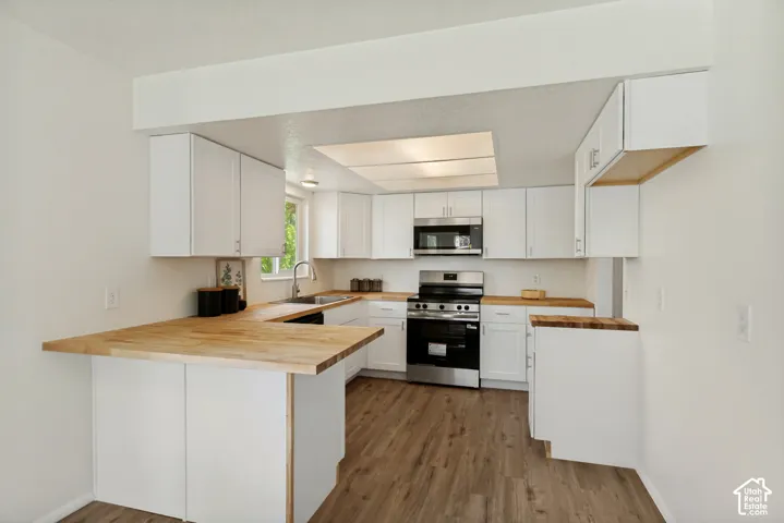 Kitchen featuring white cabinetry, wood-finish countertops, stainless steel appliances, and wood-finish flooring
