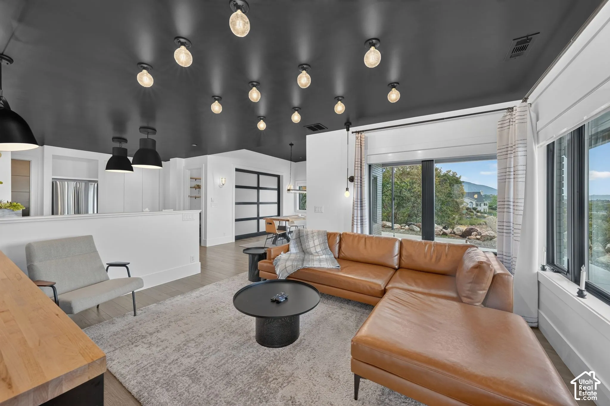 Open-concept living space featuring a dark ceiling with exposed bulb lighting, a large sliding glass door, and a built-in half-wall