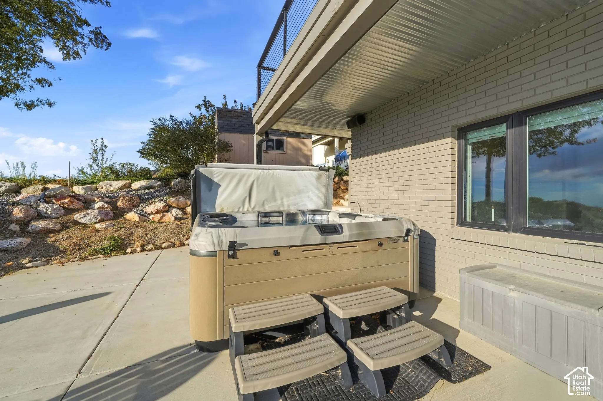 Concrete patio area featuring a built-in spa with steps, a stone retaining wall, and a brick exterior facade