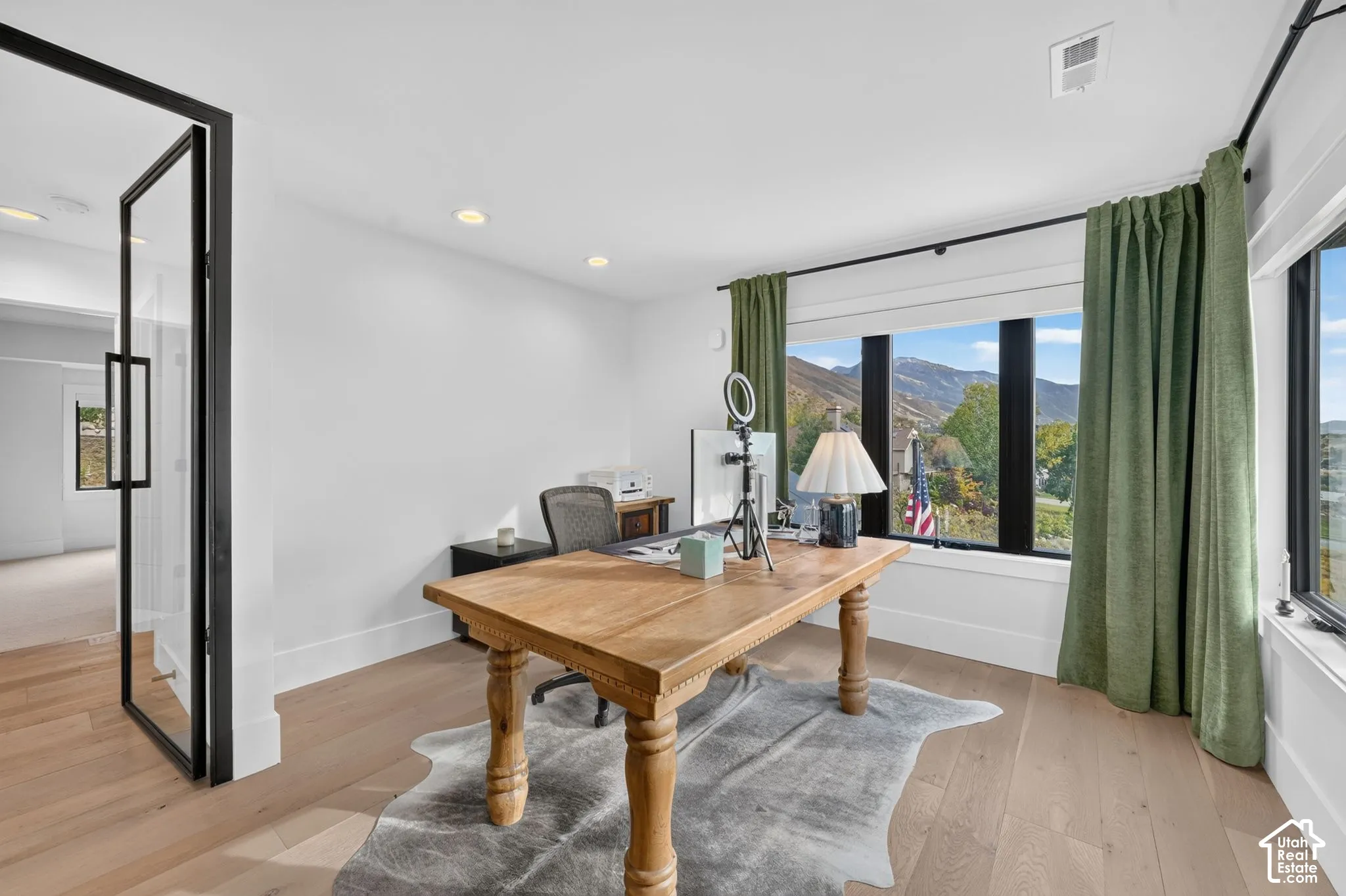 Light wood-finish flooring, recessed lighting, expansive windows with dark framing, and a full-light pivot door with dark framing