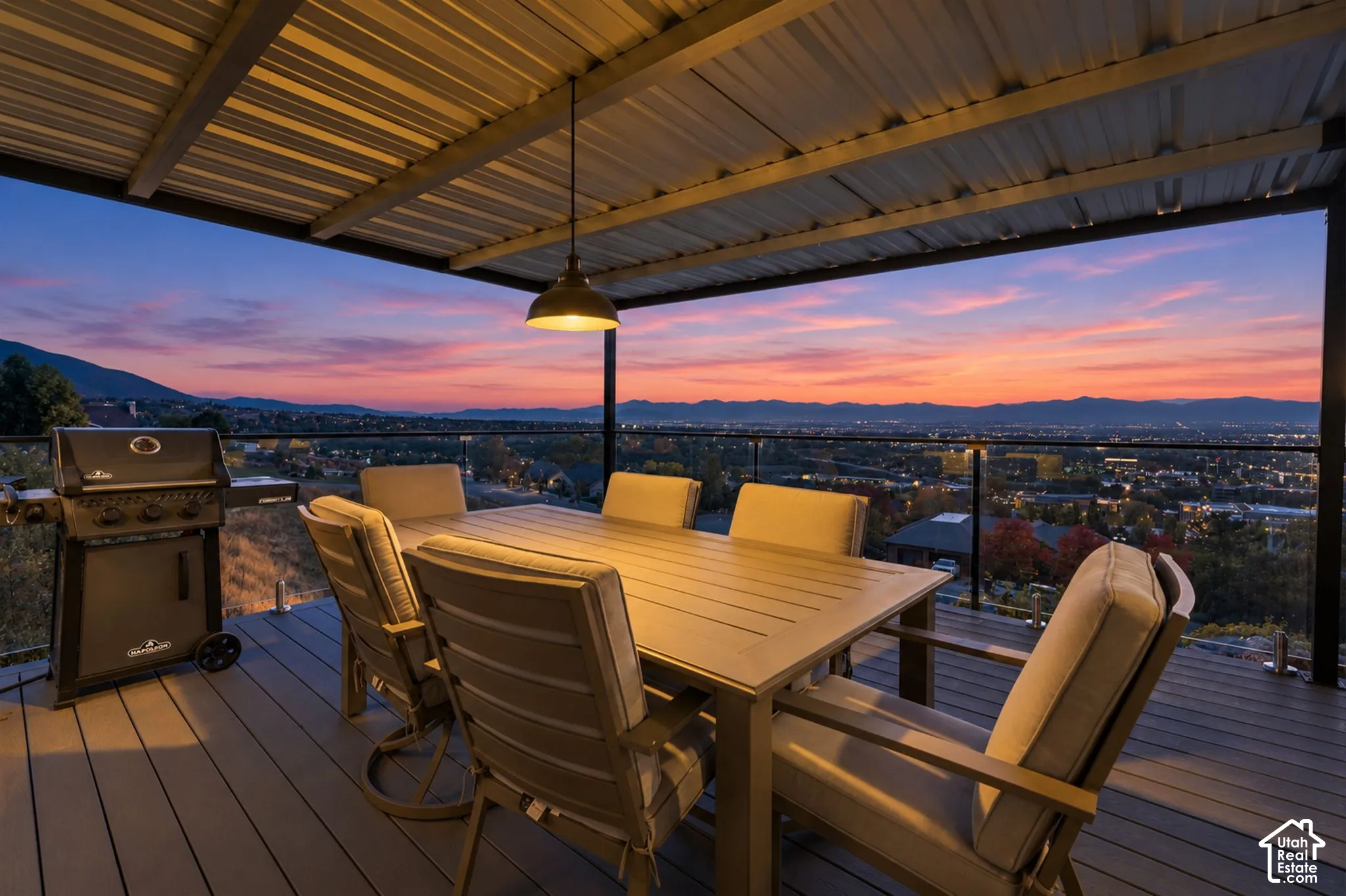 Expansive outdoor deck featuring a corrugated metal roof, suspended pendant lighting, composite decking, and glass panel railing