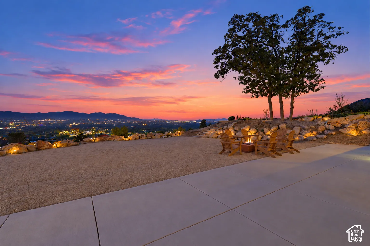 Expansive concrete patio with a built-in fire pit, surrounded by a gravel hardscape and illuminated rock landscaping