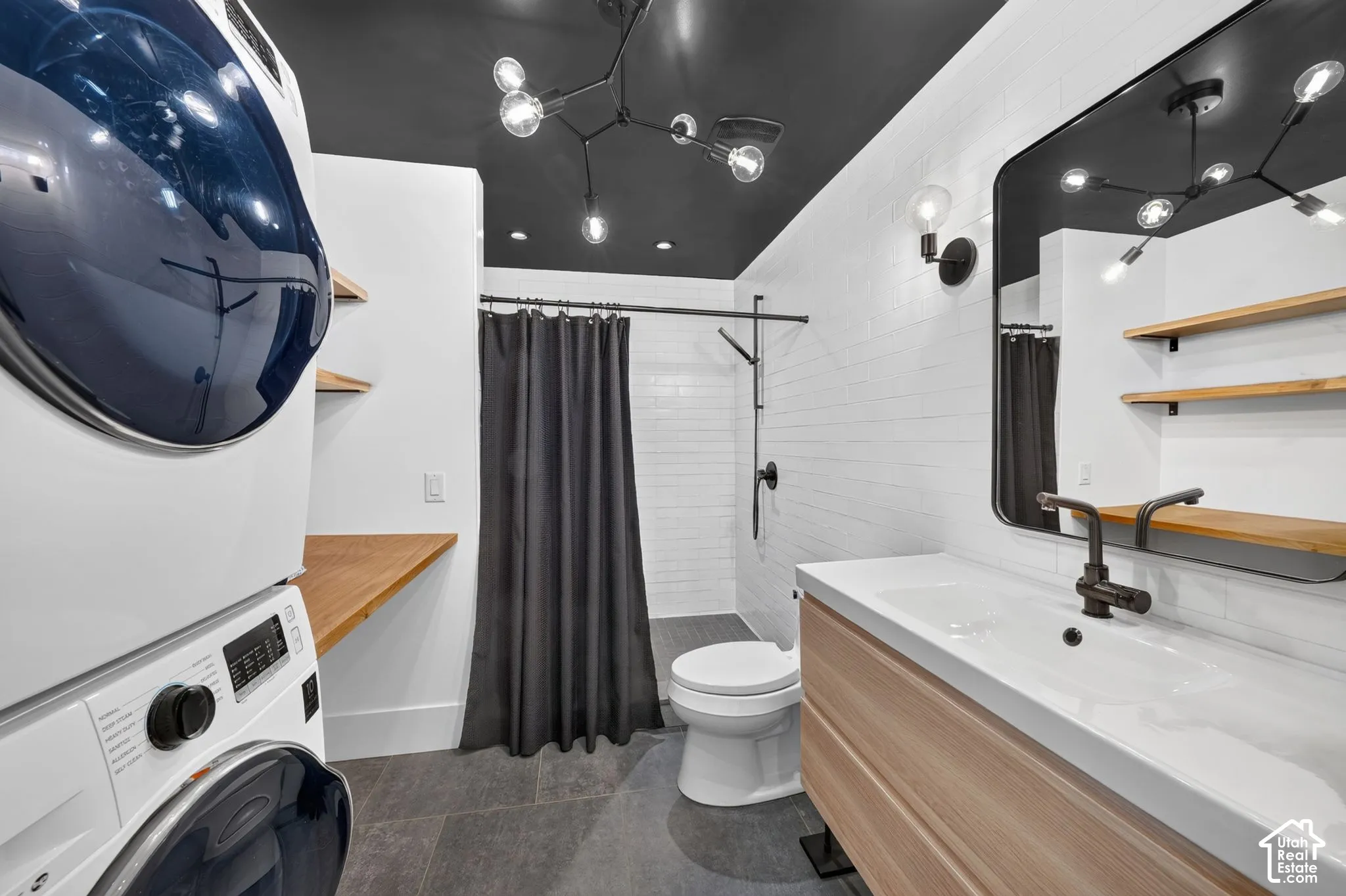 Bathroom featuring a dark ceiling, white subway tile shower surround, a wood-finish vanity with an integrated sink, and an exposed bulb chandelier