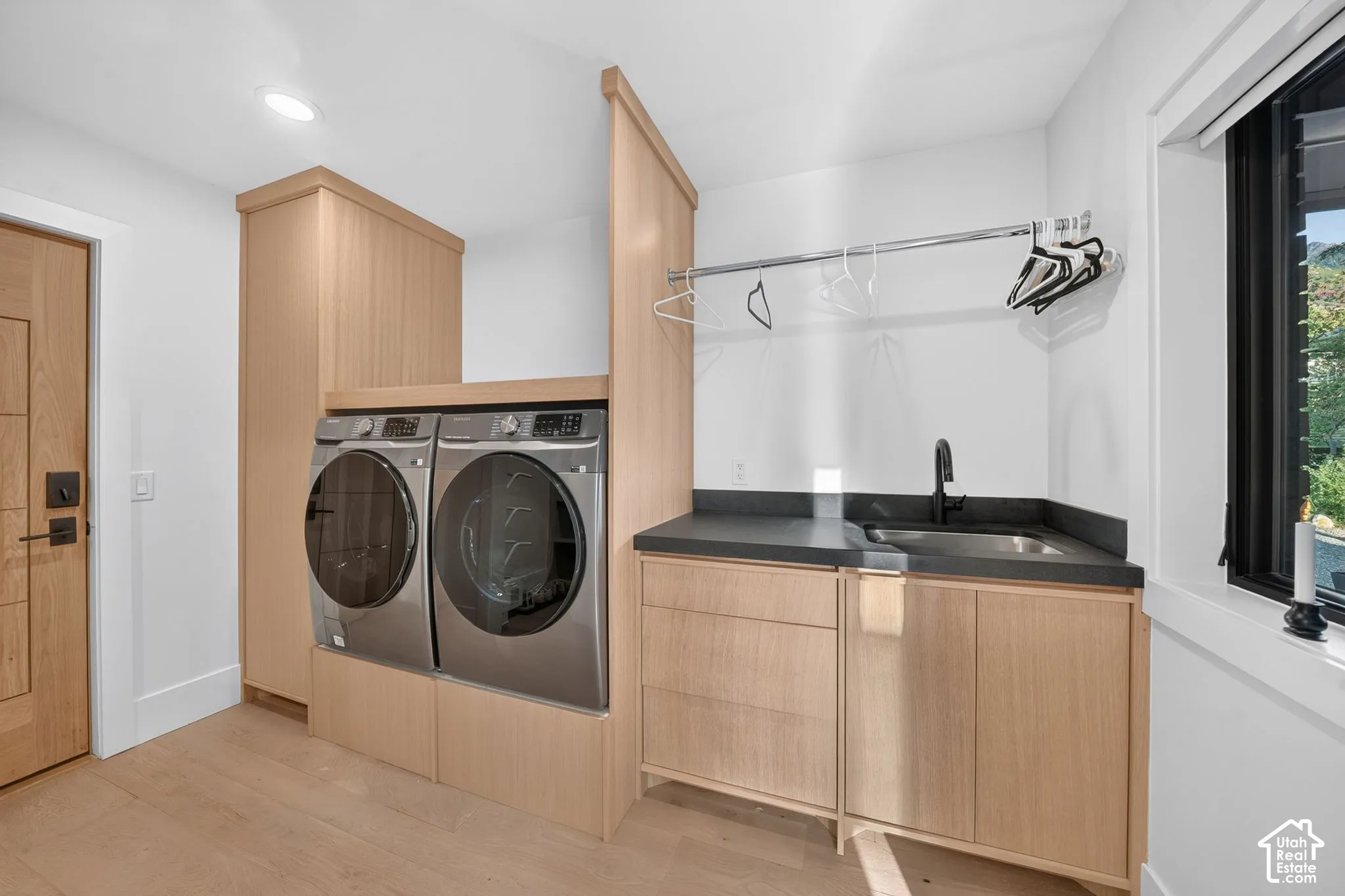 Dedicated laundry space featuring wood-finish cabinetry, a utility sink with a matte black faucet, and a hanging rod