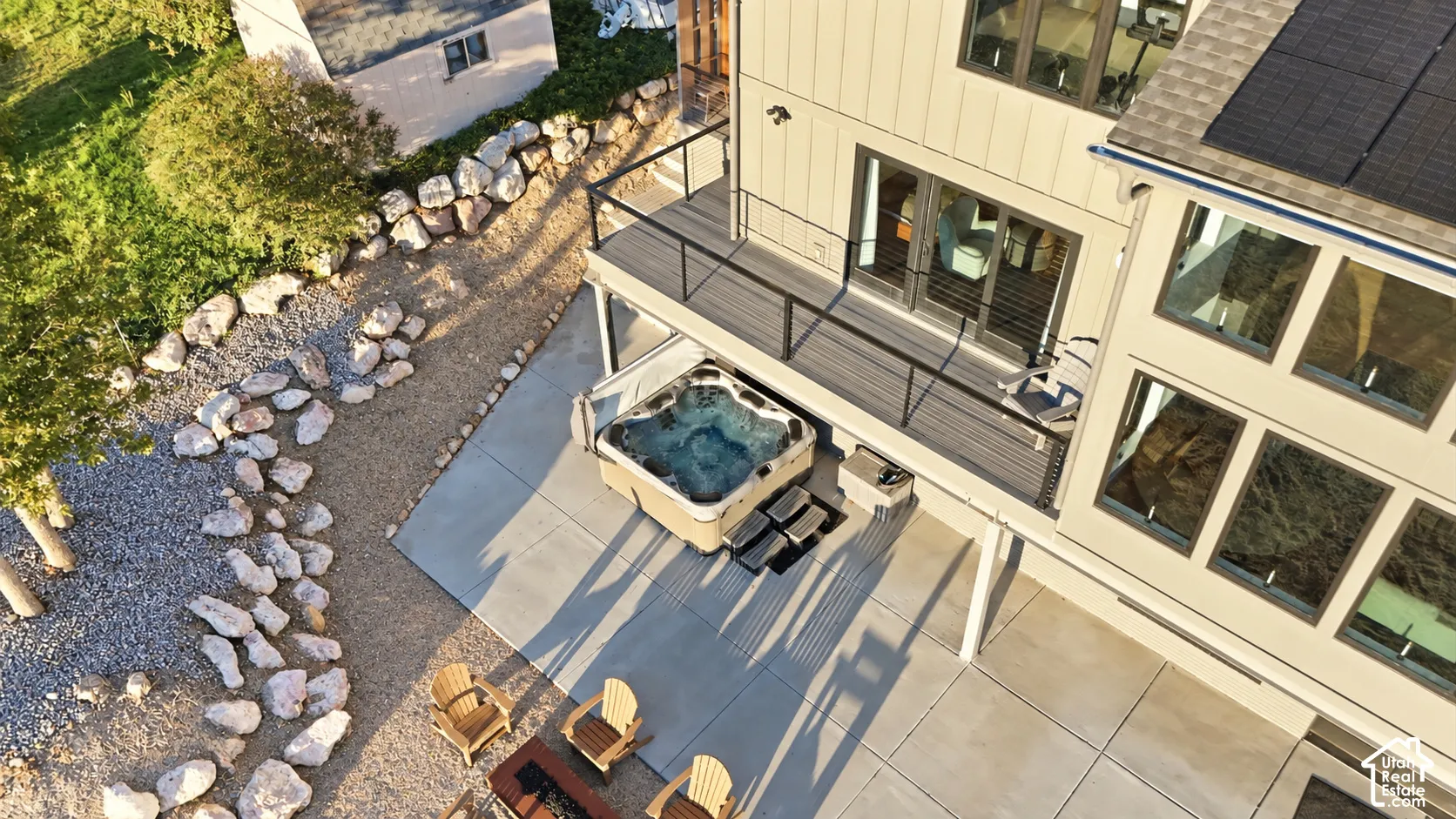 Exterior deck featuring a built-in hot tub, concrete patio, and gravel landscaping with large rocks