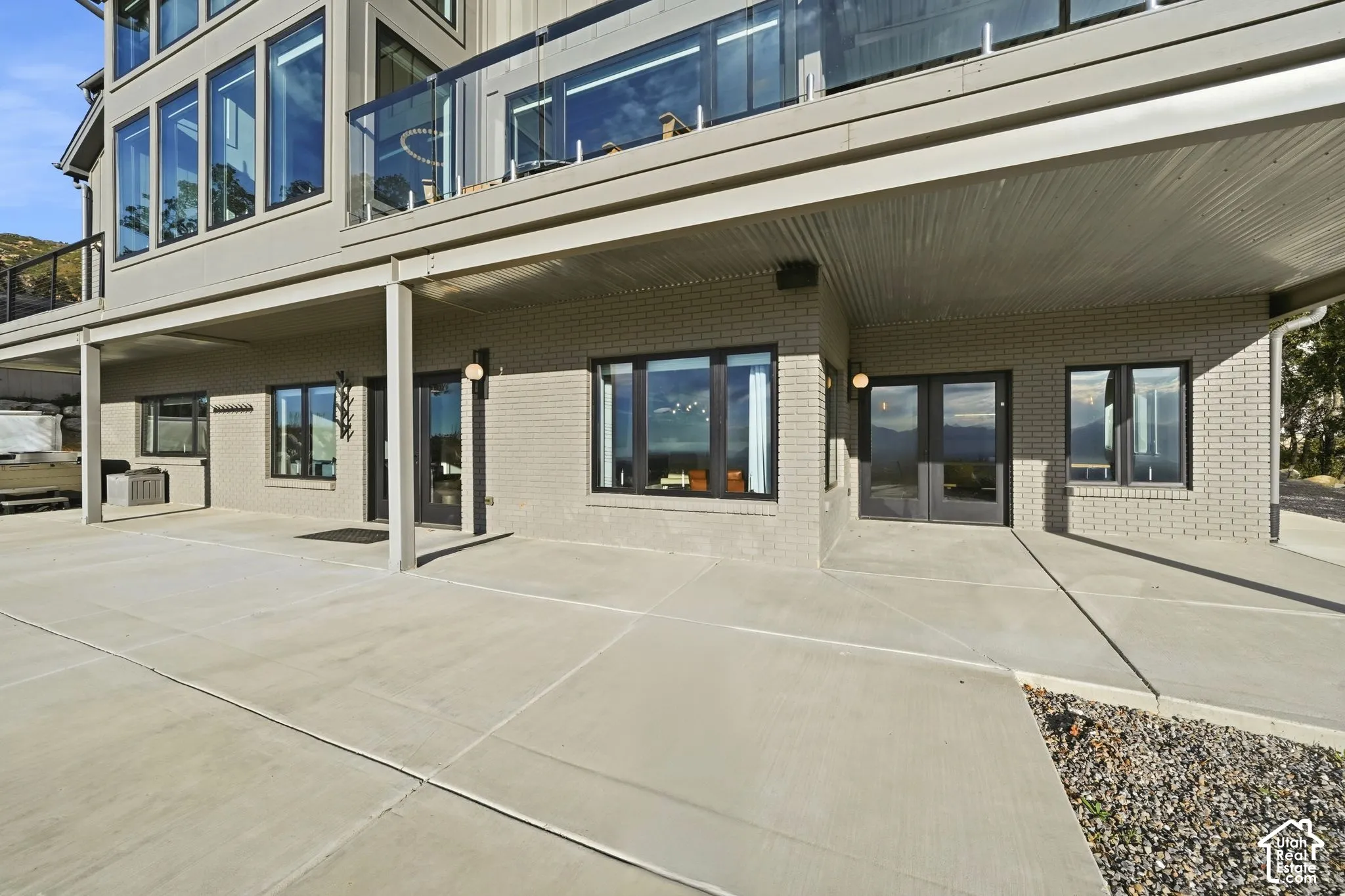 Expansive concrete patio with brick and stucco exterior, multiple large windows, and a glass-paneled balcony