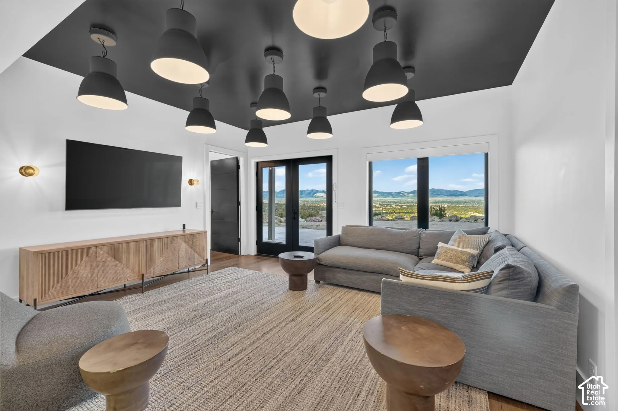 Spacious living area featuring a dark accent ceiling with multiple pendant lights, wood-finish flooring, and large windows with integrated doors