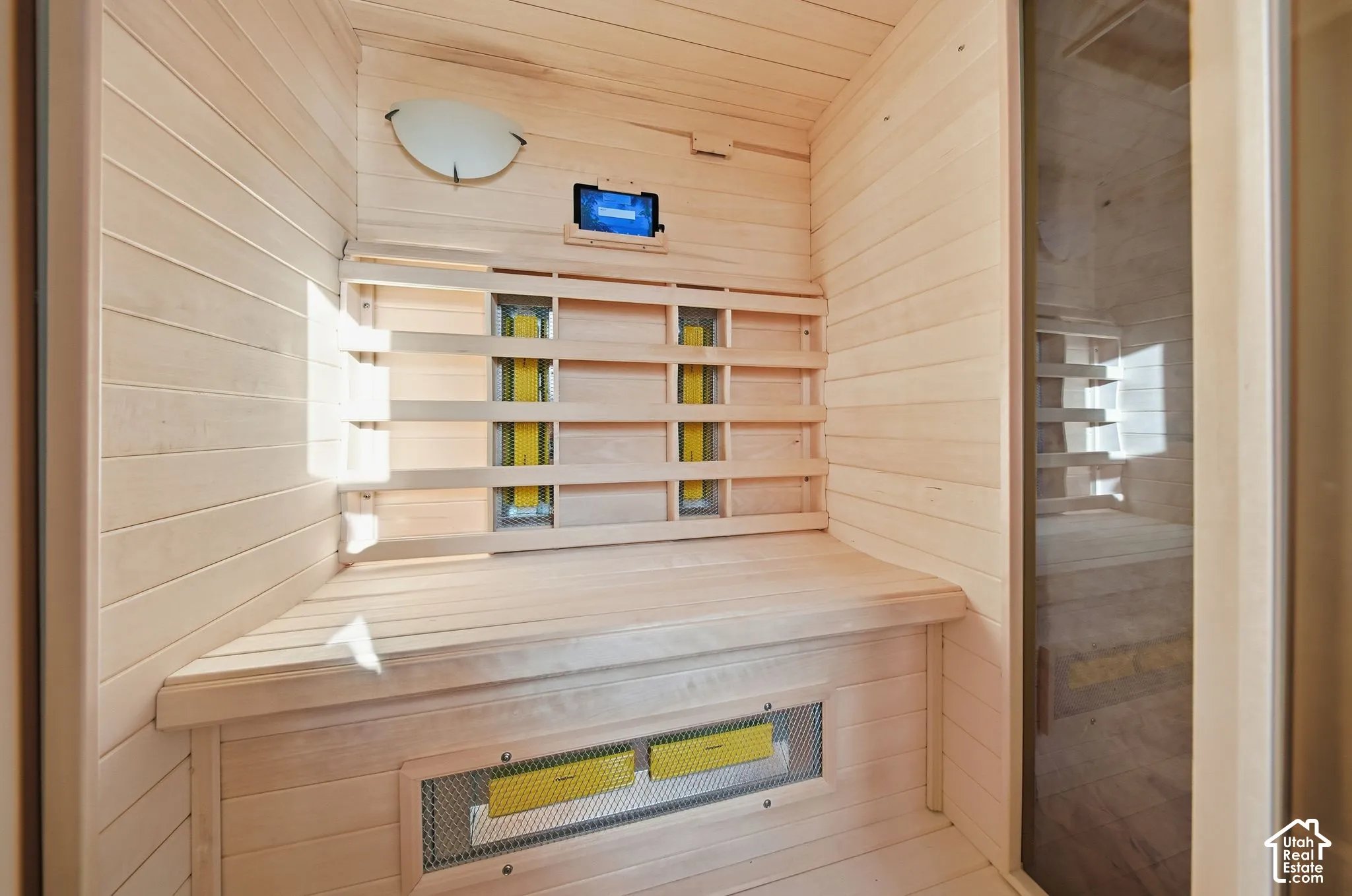 Light wood-paneled sauna featuring a built-in bench, integrated heating elements, and a glass-paneled door